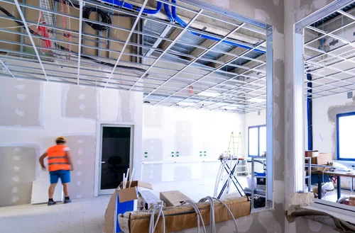 Construction worker in safety gear working on interior renovation of commercial space with exposed framing and unfinished walls, showcasing OZ General Contracting's expertise in commercial construction.