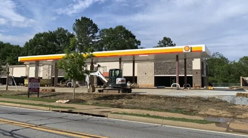 Gas station under construction with modern design elements, featuring a prominent orange and white canopy, surrounded by landscaping and construction equipment, representing OZ General Contracting's expertise in commercial renovations.