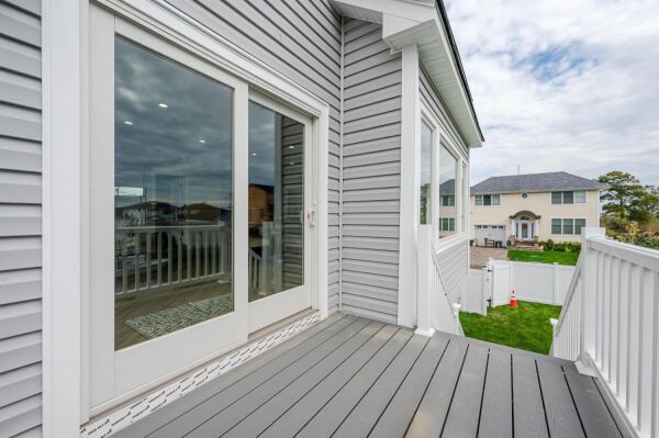 Modern home exterior with gray siding, large glass doors leading to a deck, and a view of a well-maintained yard and neighboring house, illustrating springtime renovation inspiration.