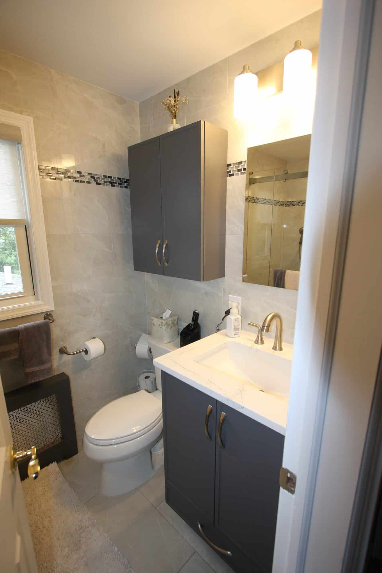Full view of the remodeled shower bathroom with navy vanity, wall cabinet above the toilet, and porcelain tile walls
