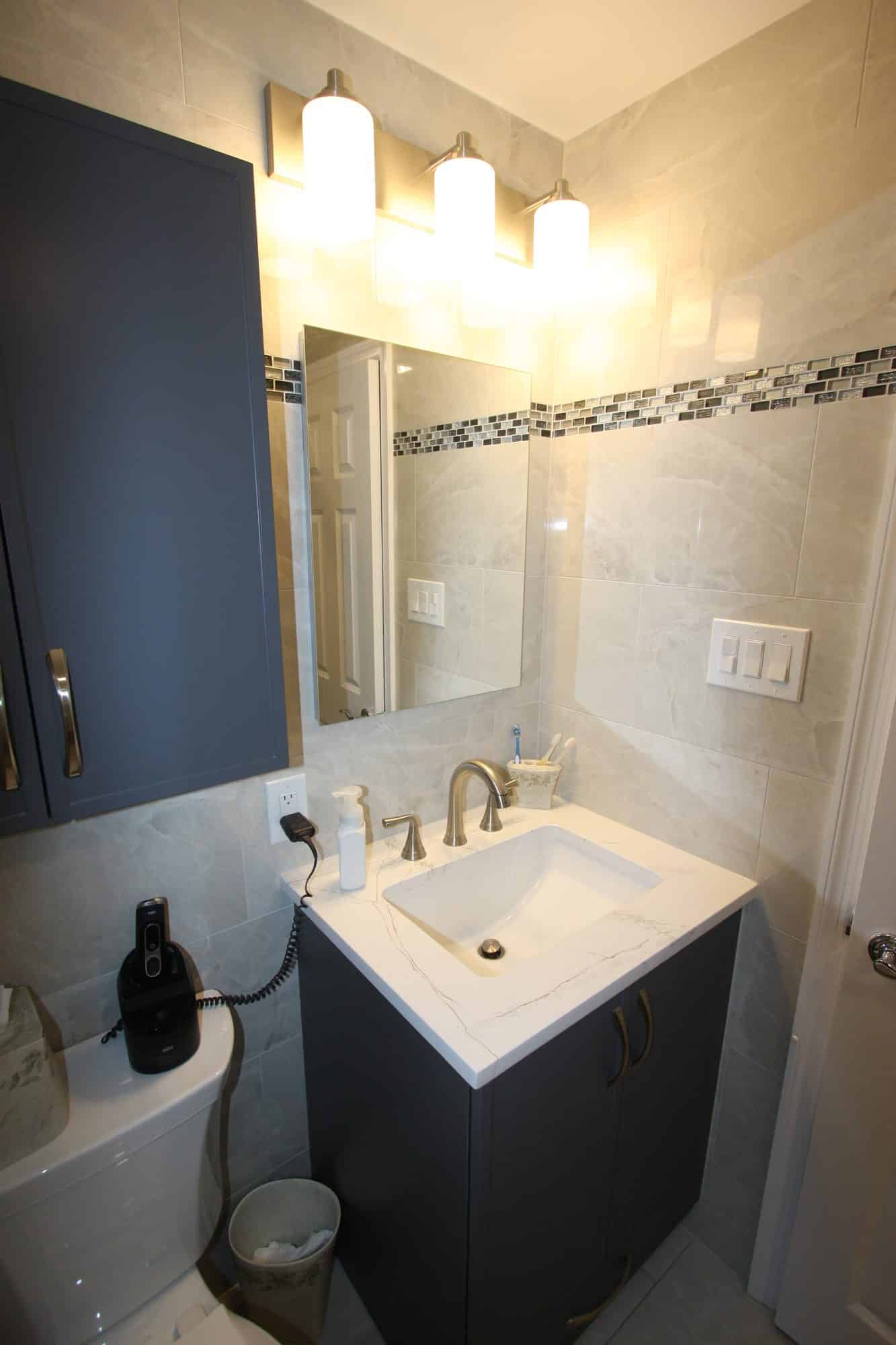 Navy vanity with white quartz top and brushed nickel faucet under a three-light fixture and mirror