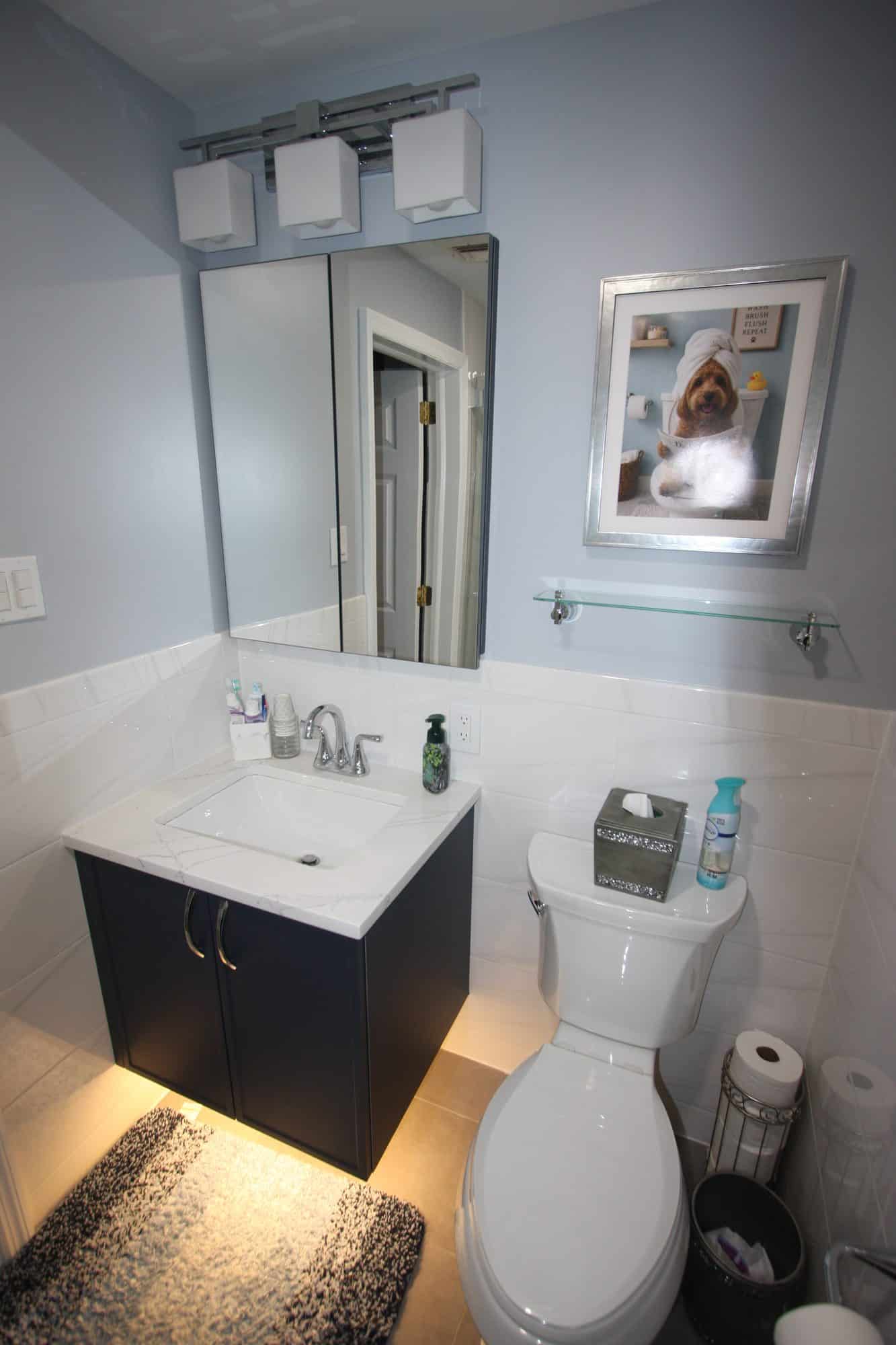 Wall-mounted navy vanity with an LED strip lighting the floor below, white tile wainscot and blue-gray walls