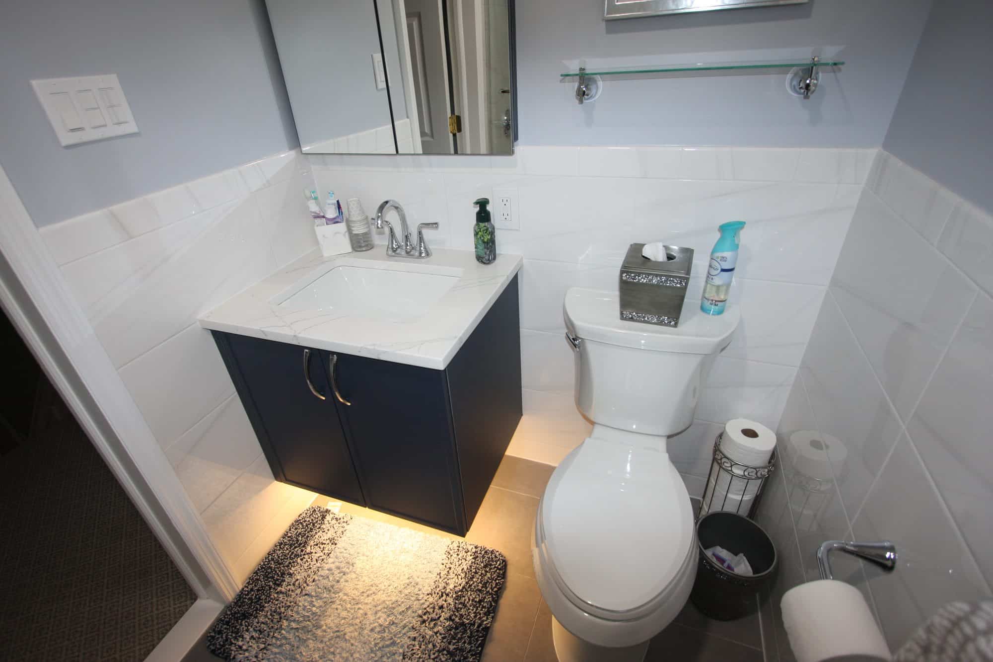 Wide view of the tub bathroom showing white tile wainscot, floating vanity, toilet and glass shelf