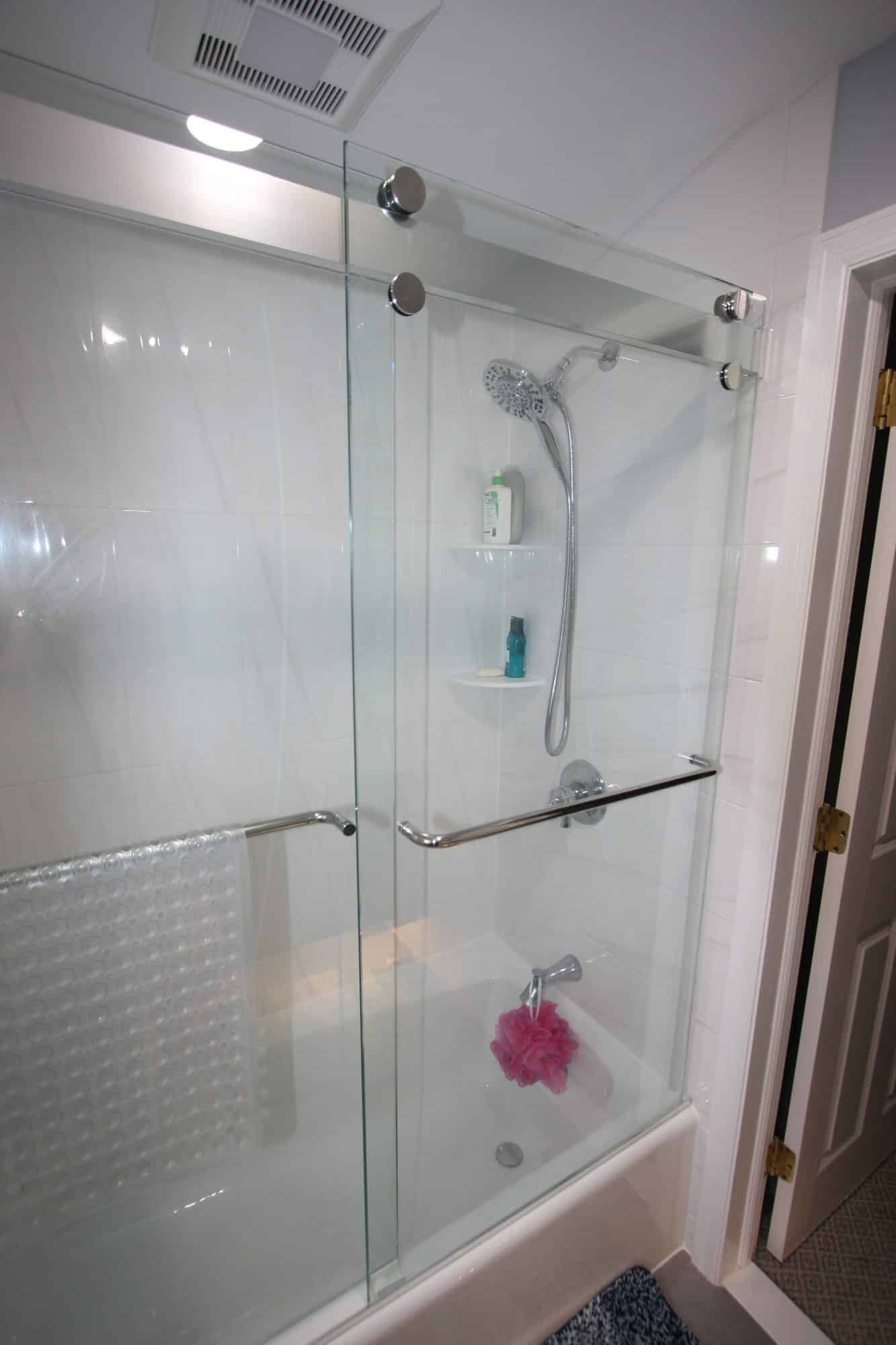 Bathtub with full-height white tile surround, handheld shower and chrome sliding glass doors