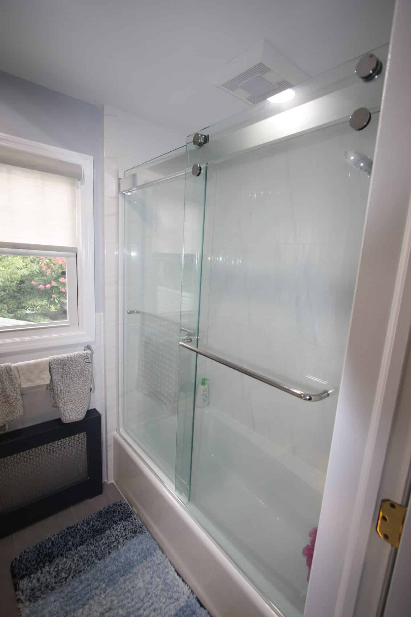 Tub enclosure beside a window, with a radiator cover and towel storage under the window