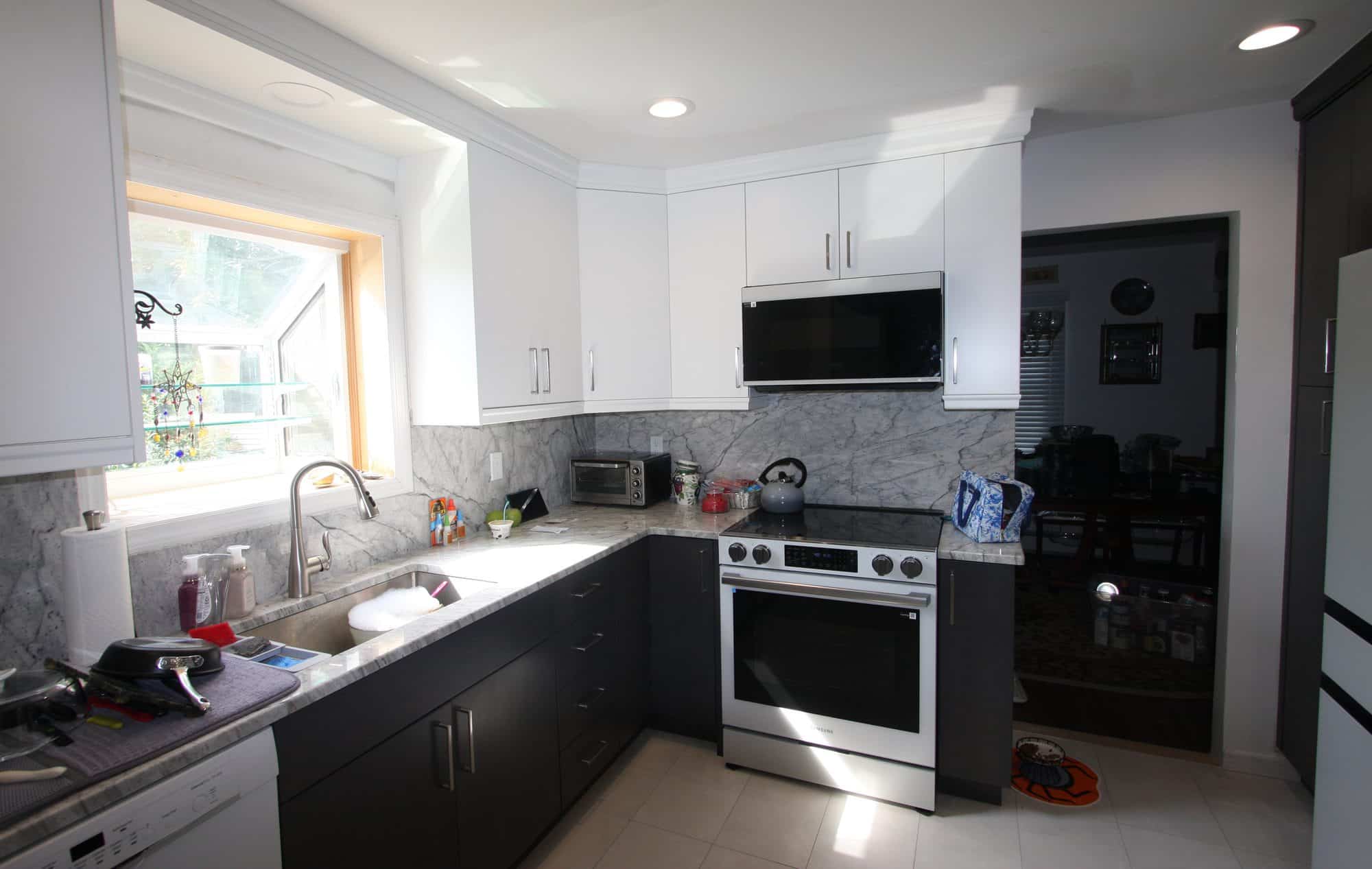 Copiague kitchen after the remodel, with white flat-panel upper cabinets, dark lower cabinets, gray-veined counters and full-height backsplash, and a stainless range