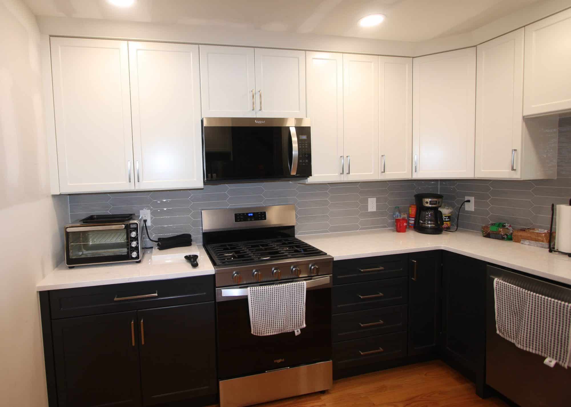 The same range wall after the remodel, with white shaker upper cabinets, charcoal lower cabinets, white quartz counters and a gray picket-tile backsplash