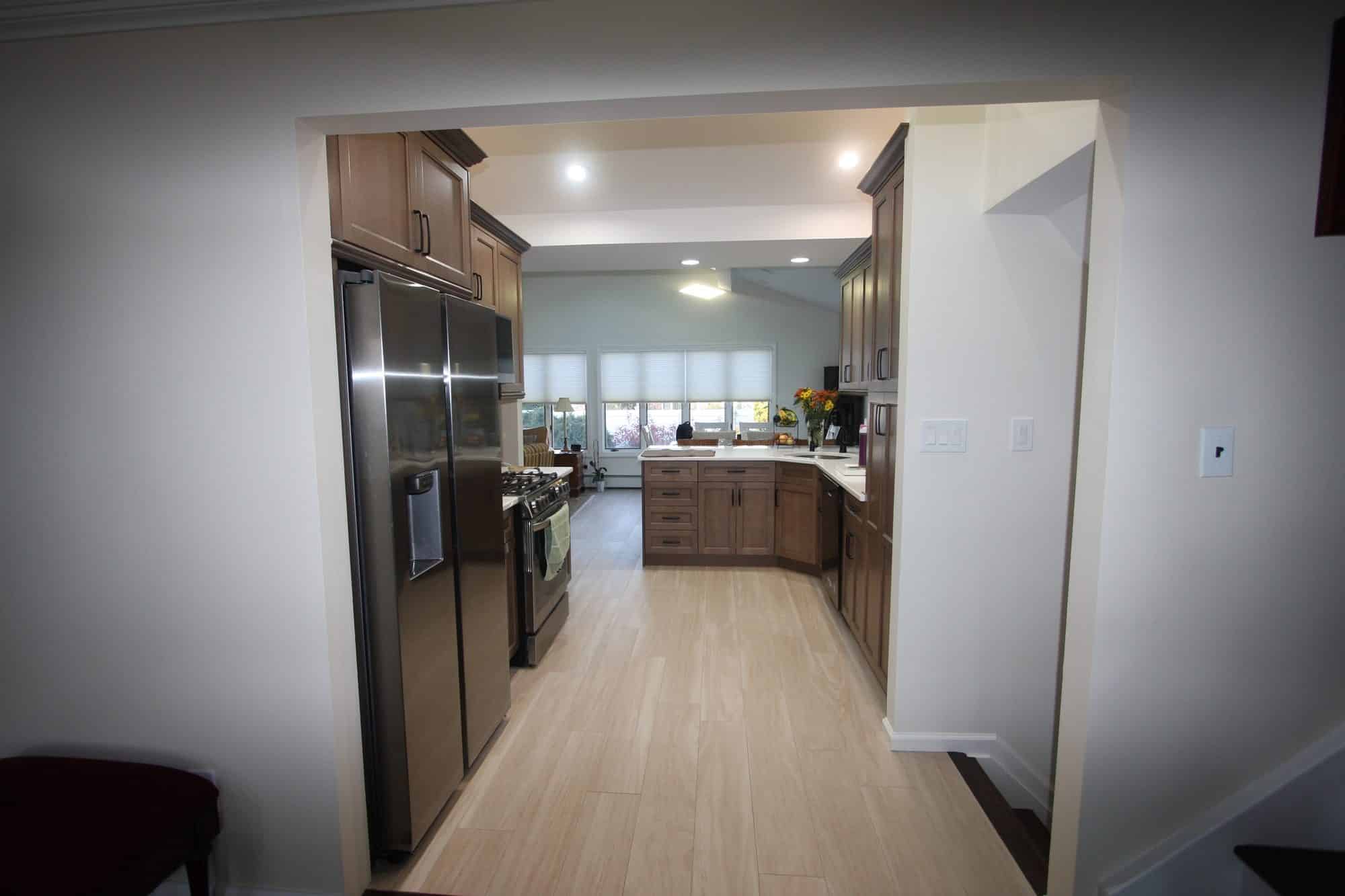 View through the kitchen entry showing the refrigerator wall, pantry run and light wood-look plank floor