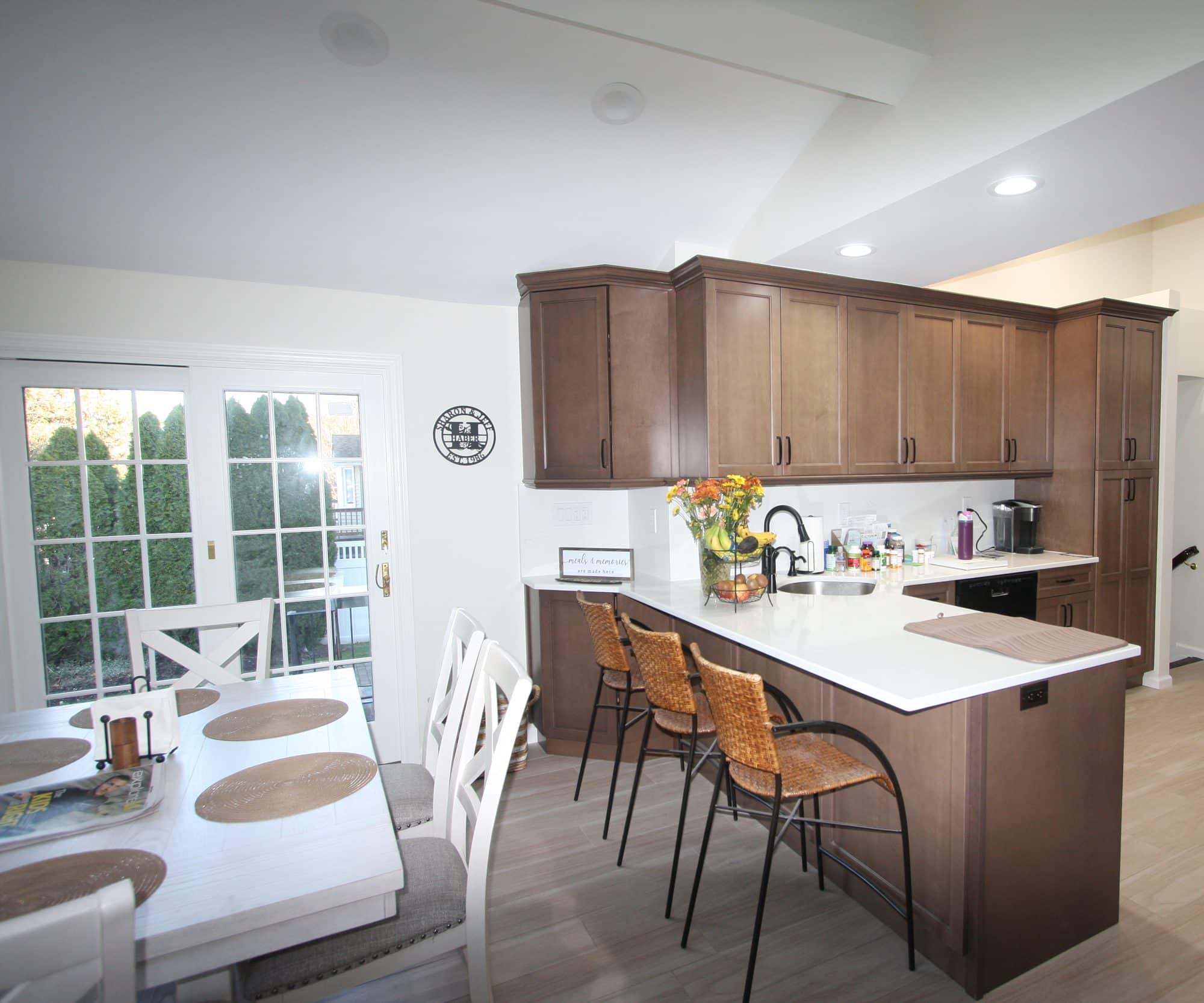 Kitchen peninsula with white quartz top and four rattan counter stools, next to French doors and a dining table