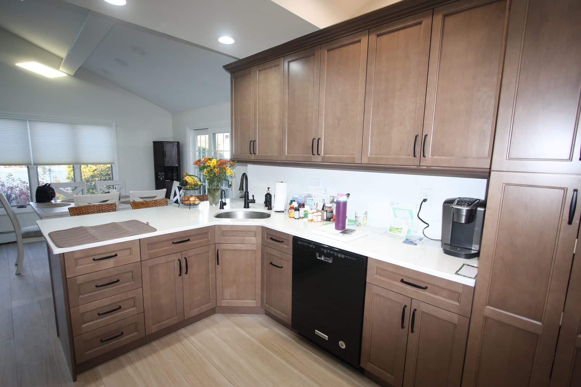 L-shaped run of stained shaker cabinets with matte black pulls, white quartz counters, a black dishwasher and an undermount sink