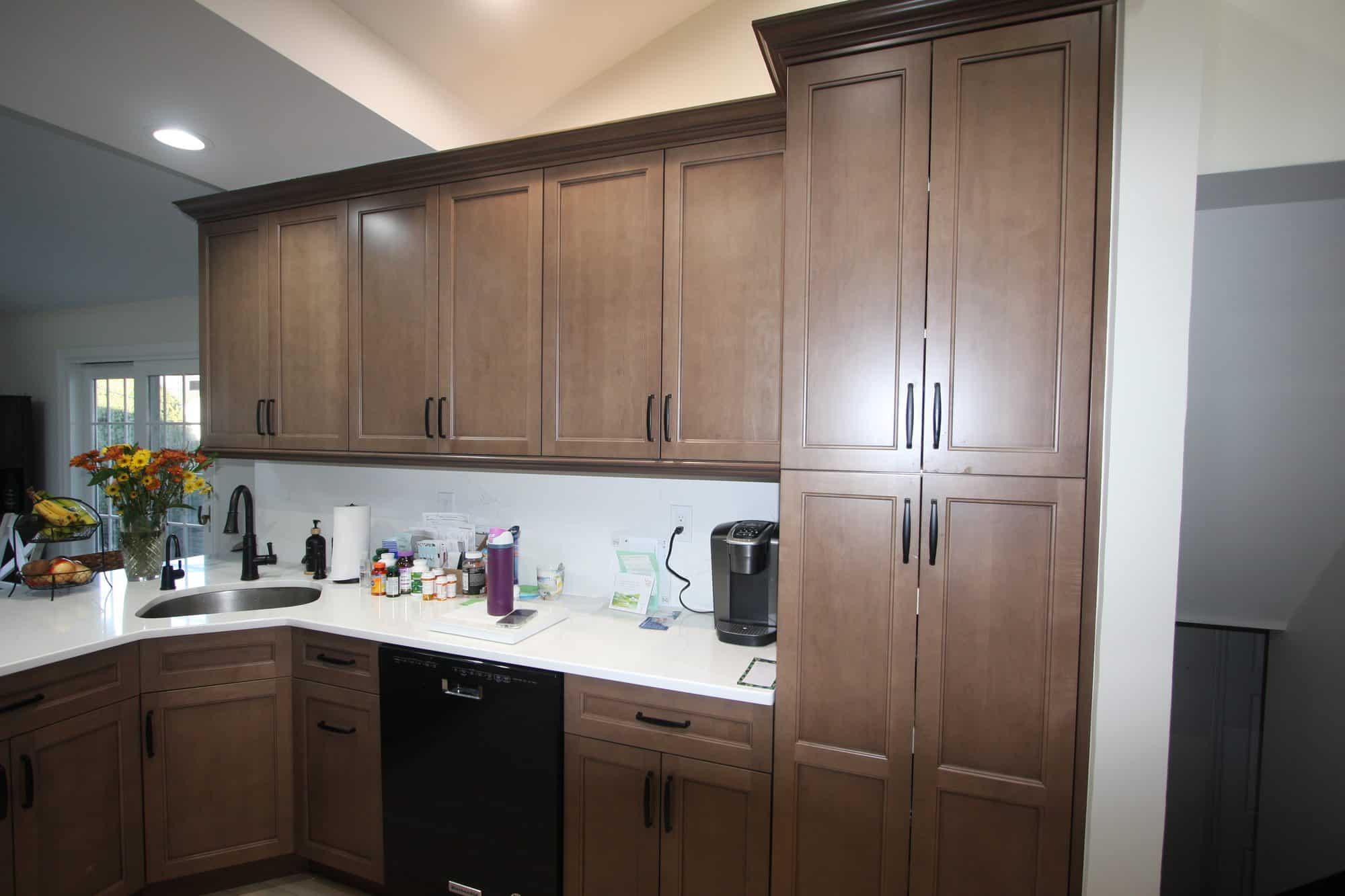 Sink wall with a floor-to-ceiling pantry cabinet, white backsplash and black pull-down faucet