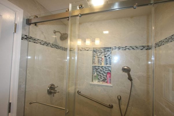 Walk-in shower with marble-look porcelain walls, a blue glass mosaic band, recessed niche and brushed nickel sliding glass door