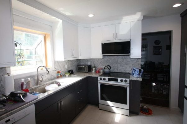 Copiague kitchen after the remodel, with white flat-panel upper cabinets, dark lower cabinets, gray-veined counters and full-height backsplash, and a stainless range