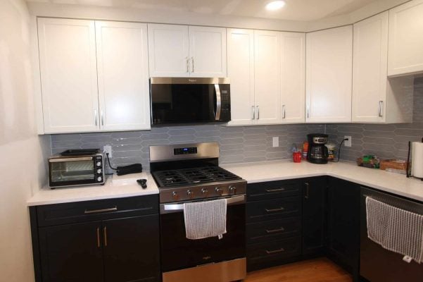 The same range wall after the remodel, with white shaker upper cabinets, charcoal lower cabinets, white quartz counters and a gray picket-tile backsplash